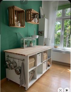 a kitchen with green walls and wooden shelves on the wall next to an open window