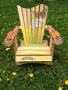 a wooden chair sitting in the grass with butterfly wings painted on it's back