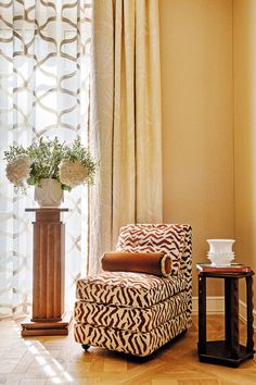 a zebra print chair in front of a window with sheer curtains and a vase filled with flowers