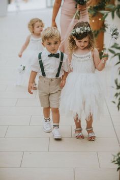 two young children are walking down the sidewalk with their mother and sister in white dresses