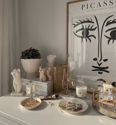 a white table topped with plates and candles next to a painting on the wall above it