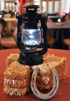 an old fashioned lantern sitting on top of hay next to a metal hook and rope