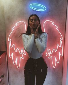 a woman standing in front of a neon sign with an angel wings design on it