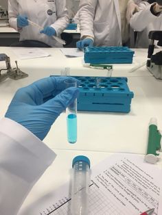 two people in white coats and blue gloves are doing experiments with test tubes on a table