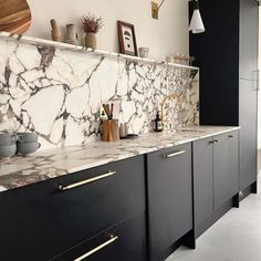 a kitchen with marble counter tops and black cabinets, gold pulls on the handles in front of it