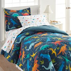 a bed with blue and orange dinosaur comforters on top of it next to a window