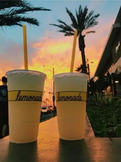 two drinks sitting on top of a table next to each other in front of a sunset