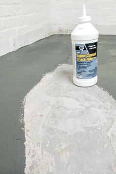 a bottle of liquid sitting on top of a cement slab next to a white brick wall