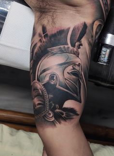 a man's leg with a helmet and feathers tattoo design on it, sitting on a bed