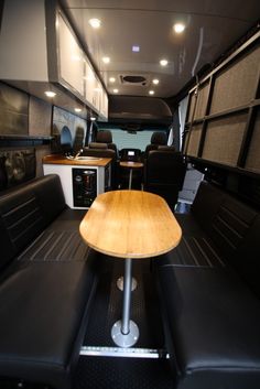 the interior of a bus with black seats and wooden table