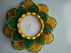 a green and yellow candle holder with a white candle in the shape of a flower