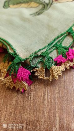 an embroidered piece of cloth with pink and green flowers on the edges, sitting on a wooden surface