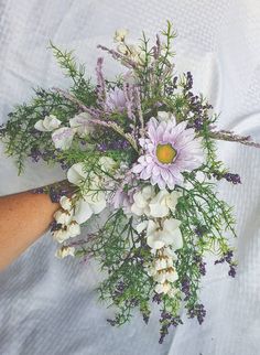 a person holding a bouquet of flowers on top of a white cloth covered tablecloth