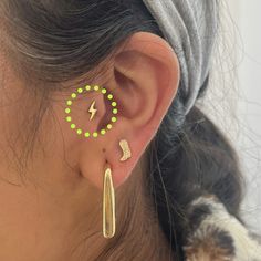 a woman wearing ear piercings with green dots and lightning bolt on the back of her ear