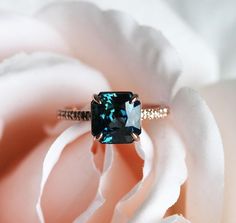 a blue diamond ring sitting on top of a white rose