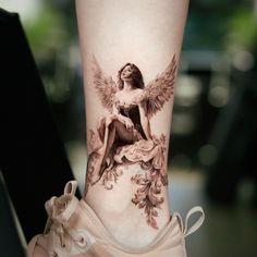 a tattoo on the leg of a woman with an angel sitting on top of it