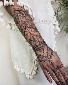 a woman's arm and hand with hendike tattoos on it, in front of a plant