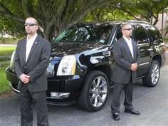 two men in suits standing next to a black suv