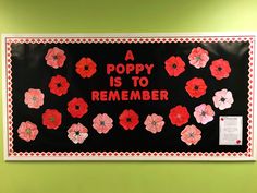 a poppy is to remember bulletin board with red and pink flowers on black paper in front of a green wall