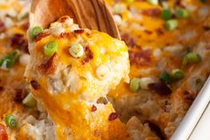 a wooden spoon scooping some food out of a casserole dish with cheese and green onions