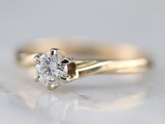 a close up view of a diamond ring on a white surface with the center stone in yellow gold