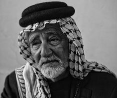 an old man wearing a black and white headdress is looking at the camera