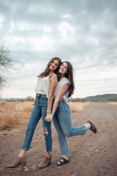 two young women are hugging in the middle of an empty road with trees and bushes behind them