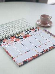 a desk with a calendar, keyboard and coffee cup