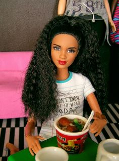 a doll is sitting at a table with a bowl of soup in front of her