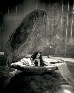 black and white photograph of a woman laying on a log in the middle of water