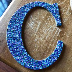 the letter c is made out of beads and sits on top of a wooden table