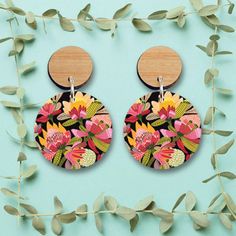 a pair of wooden earrings with floral designs on them, hanging from a green plant