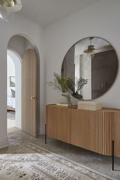 a large round mirror hangs above a wooden cabinet in the entryway to a white walled hallway