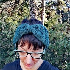 a woman wearing glasses and a knitted headband in front of some trees with no leaves