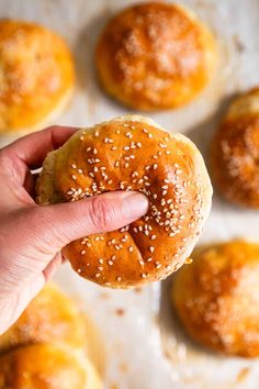 a hand holding a sesame seed bagel in front of other buns on a baking sheet