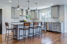 a kitchen with wooden floors and gray cabinets, white counter tops and bar stools