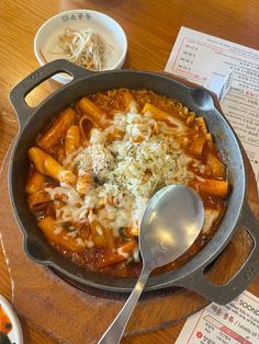 a skillet filled with pasta and cheese on top of a wooden table next to bowls of noodles