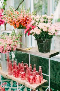 pink and white flowers are in vases on a shelf next to red glass bottles