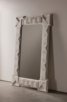 a white mirror sitting on top of a floor next to a wall with an arrow shaped frame