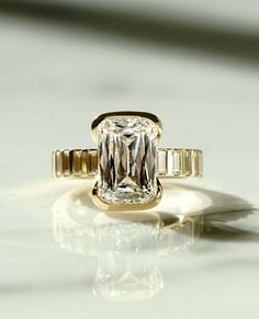 an engagement ring with a large diamond surrounded by baguettes on a reflective surface