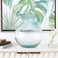 a glass vase sitting on top of a white table next to a book and flowers