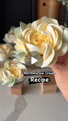 a hand holding a fake flower in front of some other flowers on a table with the words marshmallow cream recipe below it