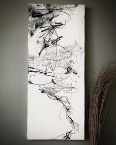 a black and white painting sitting on top of a wall next to a dry plant