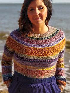 a woman is standing on the beach with her hands in her pockets and looking at the camera