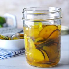 a glass jar filled with yellow liquid next to a bowl of fruit on a table