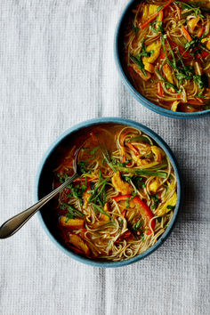 two bowls filled with noodles and vegetables on top of a white table cloth next to each other