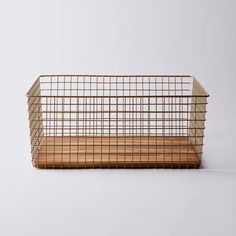 a metal basket sitting on top of a wooden shelf next to a white wall and floor