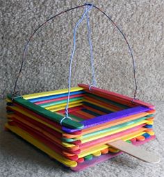 a multicolored wooden basket hanging from a string on top of a carpet floor