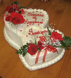 two heart shaped cakes sitting on top of a wooden table covered in frosting and roses