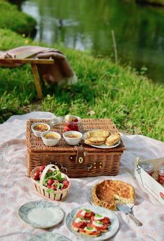 a picnic is set up on the grass by the water with food and drinks in baskets